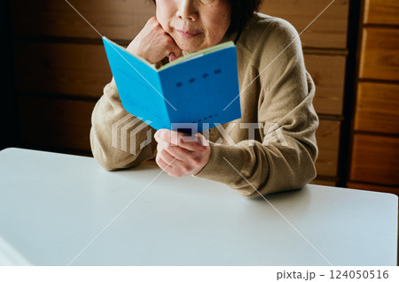 頬杖をついて年金手帳を見つめるシニア女性 124050516