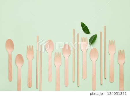 Flat lay wooden spoons, forks and straw on green background with leaves. 124051231