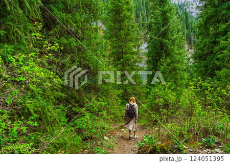 girl with black backpack walks through forest thicket in Almaty. path in coniferous thickets girl with black backpack walks through forest thicket in Almaty. path in coniferous thickets 124051395
