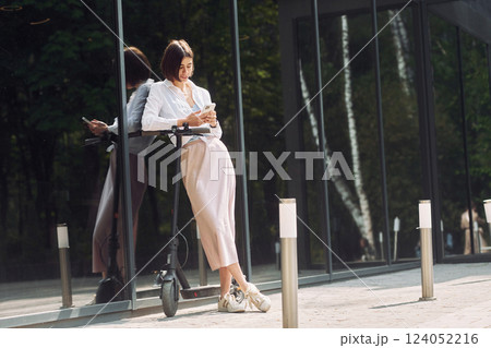 Online messaging. Beautiful young woman is with her scooter outdoors Online messaging. Beautiful young woman is with her scooter outdoors 124052216