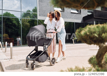 Talking and having fun. Two female friends having a walk with baby carriage outdoors Talking and having fun. Two female friends having a walk with baby carriage outdoors 124052390
