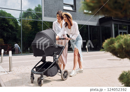 Talking and having fun. Two female friends having a walk with baby carriage outdoors Talking and having fun. Two female friends having a walk with baby carriage outdoors 124052392