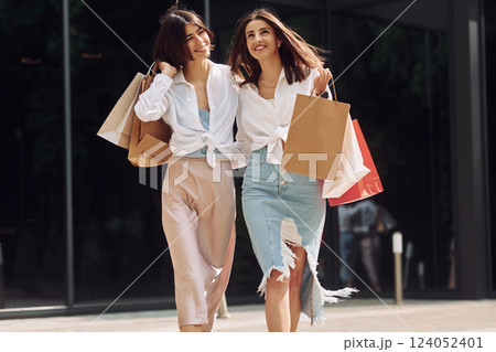 Happy buyers. Two female friends have a shopping day. Walking outdoors with bags 124052401