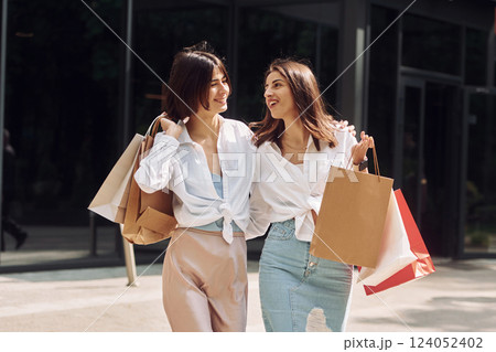 Happy buyers. Two female friends have a shopping day. Walking outdoors with bags 124052402