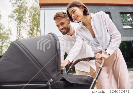 Looking at the kid. Young parents having a walk with baby carriage outdoors 124052471