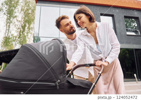 Looking at the kid. Young parents having a walk with baby carriage outdoors Looking at the kid. Young parents having a walk with baby carriage outdoors 124052472