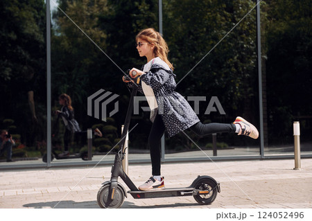 Side view. Little girl riding scooter outdoors near building outdoors 124052496