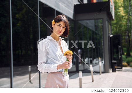 Beautiful brunette is standing outdoors with flowers in her hands Beautiful brunette is standing outdoors with flowers in her hands 124052590
