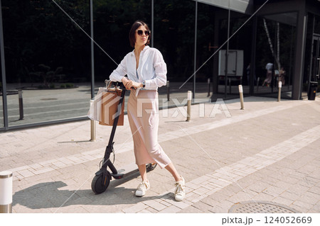 In sunglasses. Beautiful young woman is with her scooter outdoors 124052669