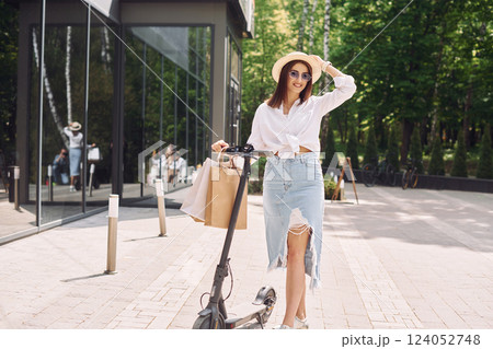Against modern building. Beautiful young woman is with her scooter outdoors Against modern building. Beautiful young woman is with her scooter outdoors 124052748