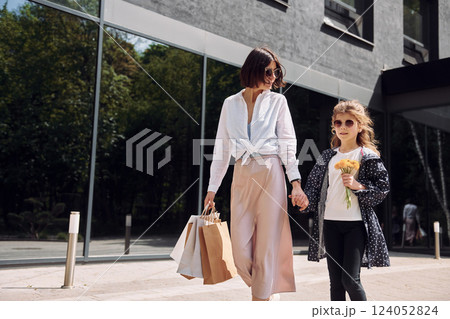 With bags in hand. Young mother with her daughter having a shopping day outdoors together 124052824