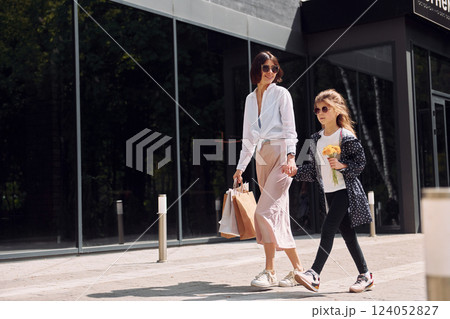 With bags in hand. Young mother with her daughter having a shopping day outdoors together 124052827