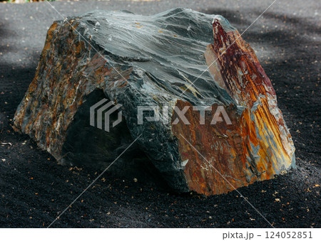 Big stone with rough corners in stone ZEN garden. A grey brown rock with sharp edges and textured surface on a racked black sand. Natural stones rocks 124052851