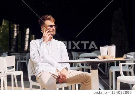 Stylish young man in sunglasses sitting on the chair of cafe outdoors 124052899