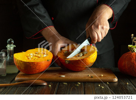 Cutting a ripe big watermelon with a knife in the hands of a skilled chef. Low key concept of cooking a national dish on the kitchen table. Cutting a ripe big watermelon with a knife in the hands of a skilled chef. Low key concept of cooking a national dish on the kitchen table. 124053721