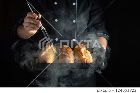 Fork and baking tray with hot buns in the hands of an experienced baker. Low-key concept of making fresh and delicious pies. 124053722