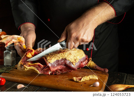 Cutting a bird carcass with a knife in the hands of an experienced chef. Working environment on the work table with spices and ingredients during the preparation of a duck. Cutting a bird carcass with a knife in the hands of an experienced chef. Working environment on the work table with spices and ingredients during the preparation of a duck. 124053723