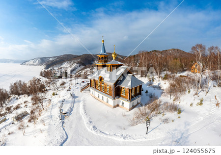 Aerial top view to wooden church of Transfiguration covered snow of the Lord on mountain near village Port Baikal. Frozen ice Lake and river Angara on backgroud. Winter landscape Siberia, Russia. Aerial top view to wooden church of Transfiguration covered snow of the Lord on mountain near village Port Baikal. Frozen ice Lake and river Angara on backgroud. Winter landscape Siberia, Russia. 124055675