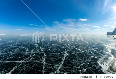 Aerial view on transparent frozen water, violet sunset in background. Beautiful winter landscape with clear blue smooth ice with cracks and mountains. Small Sea, Olkhon, Baikal lake, Siberia, Russia. Aerial view on transparent frozen water, violet sunset in background. Beautiful winter landscape with clear blue smooth ice with cracks and mountains. Small Sea, Olkhon, Baikal lake, Siberia, Russia. 124055695