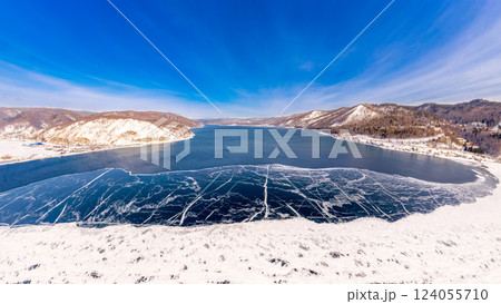 Aerial top view to Blue clear ice lake Baikal. Crack covered snow on frozen water surface. Cold winter landscape with mountains, sunny day, Natural background. , Russia, Siberia. Aerial top view to Blue clear ice lake Baikal. Crack covered snow on frozen water surface. Cold winter landscape with mountains, sunny day, Natural background. , Russia, Siberia. 124055710