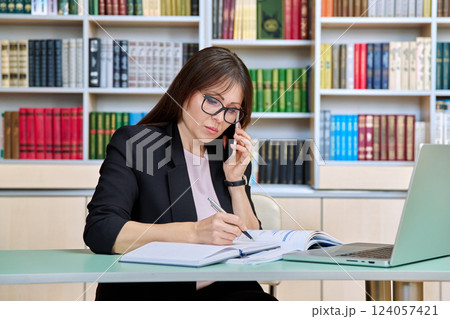 Middle aged female teacher working inside library office with laptop 124057421