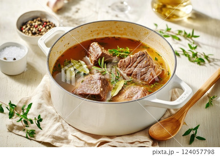 Hearty beef stew simmering in a white pot with fresh herbs and spices on a kitchen counter Hearty beef stew simmering in a white pot with fresh herbs and spices on a kitchen counter 124057798