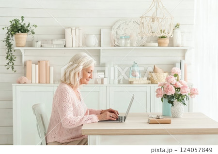 Elderly woman working on laptop at a cozy home office with floral decor and natural light Elderly woman working on laptop at a cozy home office with floral decor and natural light 124057849