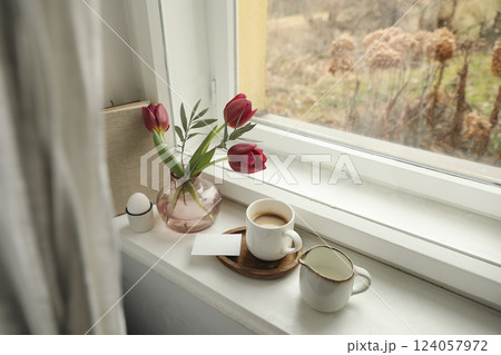 Easter spring still life. Cup of coffee, floral bouquet on window sill. Red tulips flowers, olive branches in vase. Milk pitcher, egg. Business card mockup. Home decor, breakfast. Scandinavian 124057972