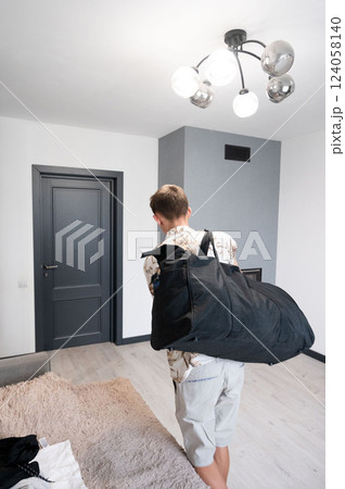 Person carrying a large black bag in a stylish modern living space with bright lighting and contemporary decor while preparing to leave 124058140