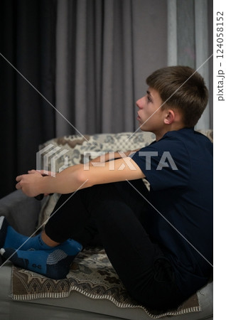 Young boy deeply focused on a screen, sitting on a cozy couch in a softly lit living room during a quiet evening at home Young boy deeply focused on a screen, sitting on a cozy couch in a softly lit living room during a quiet evening at home 124058152