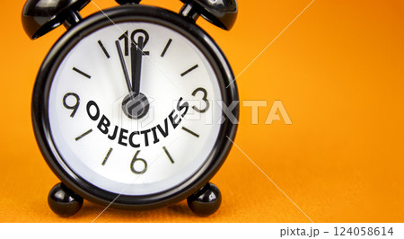 Objectives symbol. Concept word Objectives on beautiful orange paper. Beautiful orange paper background. Black alarm clock. Business objectives concept. Copy space. 124058614