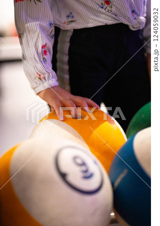 Hand reaching for vibrant bowling ball in colorful, well-lit bowling alley with various balls and blurred background creating dynamic atmosphere 124059032