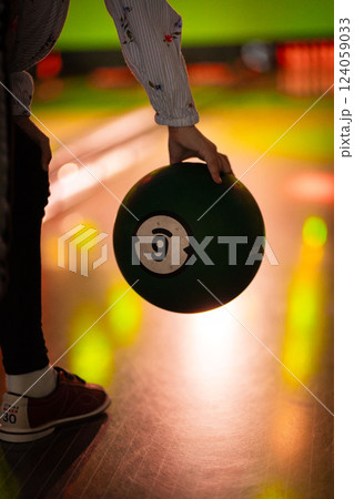Hand reaching for vibrant bowling ball in colorful, well-lit bowling alley with various balls and blurred background creating dynamic atmosphere 124059033