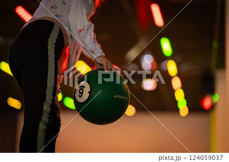 Hand reaching for vibrant bowling ball in colorful, well-lit bowling alley with various balls and blurred background creating dynamic atmosphere 124059037