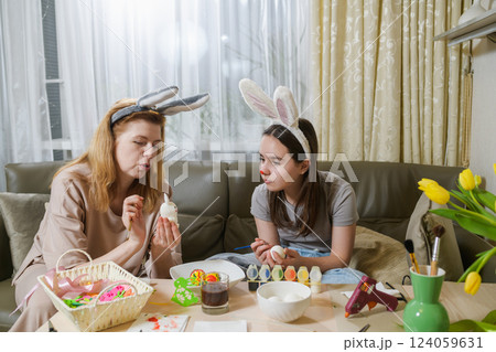 A mother and daughter wearing bunny ears decorating Easter eggs with paint and brushes. A mother and daughter wearing bunny ears decorating Easter eggs with paint and brushes. 124059631