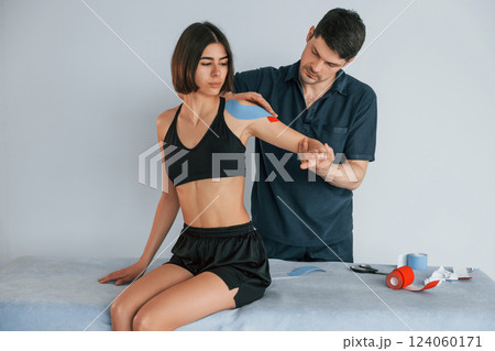 On the left hand. Woman visiting physiologist that putting kinesio tape on the skin On the left hand. Woman visiting physiologist that putting kinesio tape on the skin 124060171