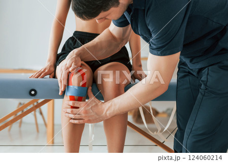 Working with legs. Woman visiting physiologist that putting kinesio tape on the skin 124060214