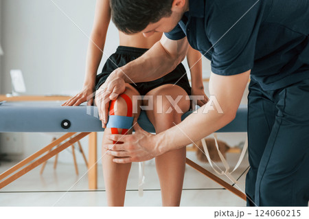 Working with legs. Woman visiting physiologist that putting kinesio tape on the skin 124060215