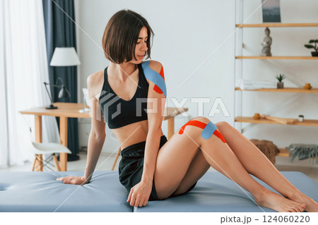 Sitting on the table. Woman with kinesio tape is in the clinic indoors 124060220