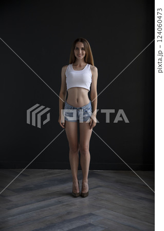 young girl in a t-shirt and shorts on a dark background, full length studio shot 124060473