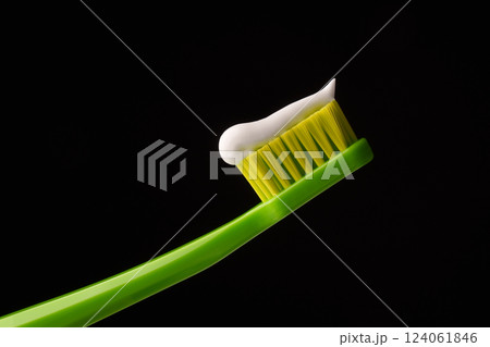 Green plastic toothbrush with white toothpaste on a black background. Professional photo. 124061846