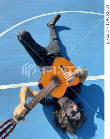 Man Lying On The Ground Plays Classical Guitar On Blue Floor Outdoor 124062633