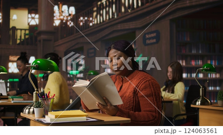 African american professor preparing her learning materials and resources in the library, leveraging expertise to mentor scholars and create a productive academic atmosphere for pupils. Camera B. 124063561