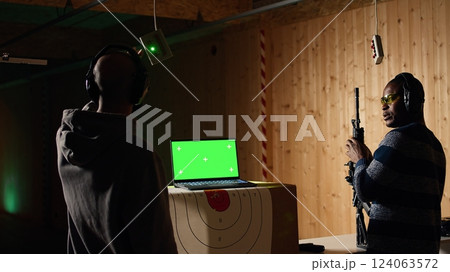 Green screen laptop next to shooting gallery safety officer watching client shoot at targets, supervising him. Mockup notebook and firing range expert teaching man how to use firearms, camera A Green screen laptop next to shooting gallery safety officer watching client shoot at targets, supervising him. Mockup notebook and firing range expert teaching man how to use firearms, camera A 124063572