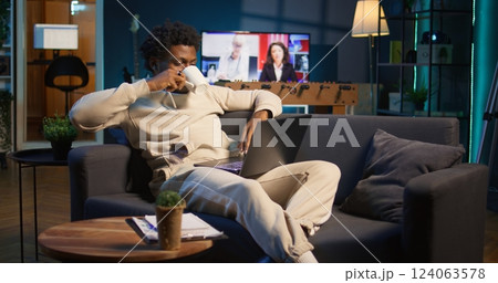 Positive african american man multitasking on a laptop in stylish loft, fully connected to the internet while managing his freelance work and remote responsibilities. Browsing web at home. Camera B. Positive african american man multitasking on a laptop in stylish loft, fully connected to the internet while managing his freelance work and remote responsibilities. Browsing web at home. Camera B. 124063578