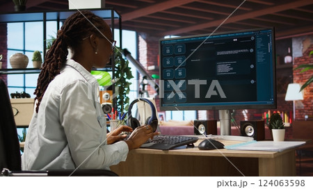 Woman seated at desk using AI LLM chatbot software in modern urban home office. Person requesting help from large language model program on computer in bright apartment workspace, camera A 124063598