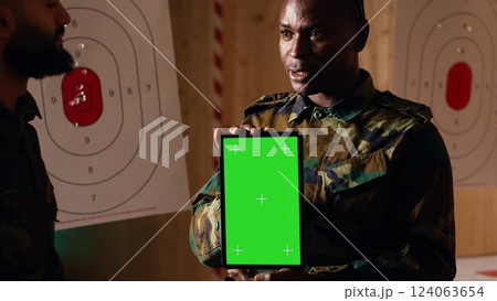 Team of military units at shooting range watching video on green screen tablet to learn necessary combat skills. Army soldiers looking at instructions on chroma key device during training, camera B Team of military units at shooting range watching video on green screen tablet to learn necessary combat skills. Army soldiers looking at instructions on chroma key device during training, camera B 124063654