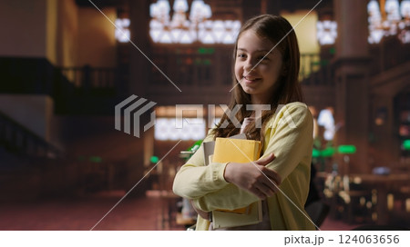 Portrait of sweet preadolescent carrying her books and class notes in the library, preparing for an intense studying session with her textbooks. Academic environment to ensure development. Camera B. Portrait of sweet preadolescent carrying her books and class notes in the library, preparing for an intense studying session with her textbooks. Academic environment to ensure development. Camera B. 124063656