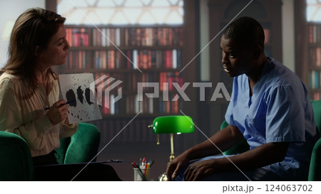 Counselor presents a Rorschach test to a medical assistant in uniform, looking for answers with psychoanalysis illustration. Nurse suffering from PTSD and trauma, interpretation therapy. Camera B. Counselor presents a Rorschach test to a medical assistant in uniform, looking for answers with psychoanalysis illustration. Nurse suffering from PTSD and trauma, interpretation therapy. Camera B. 124063702