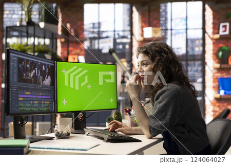 Woman video creator edits a multimedia project next to chroma key at agency office, using professional tech tools and editing software to manage timeline editing and video production. 124064027